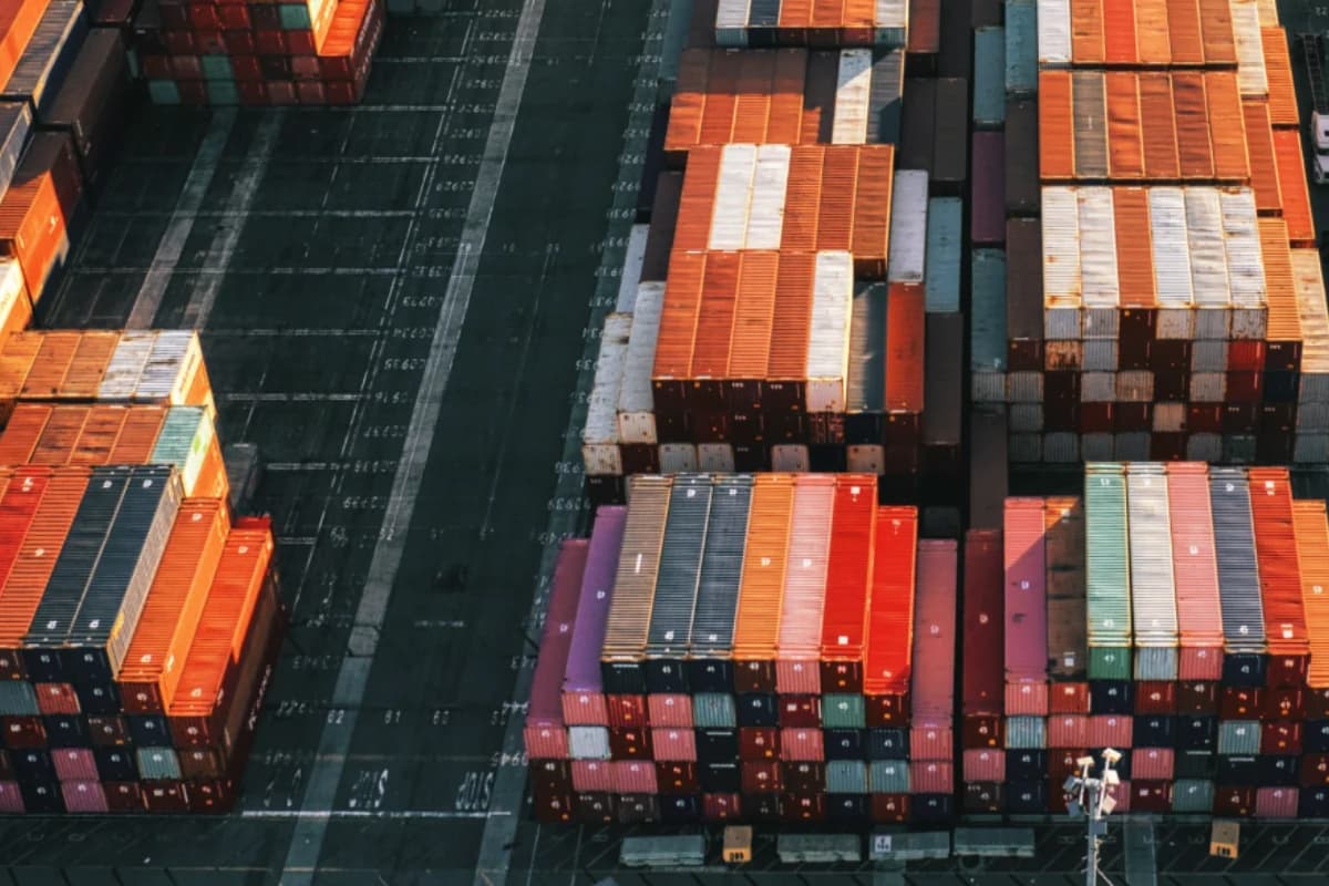 Pomarańczowe, białe i granatowe kontenery oraz pasy transportowe widziane z góry.