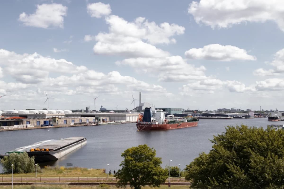 Statek na kanale portowym, zabudowania nabrzeża i chmury nad wodą.